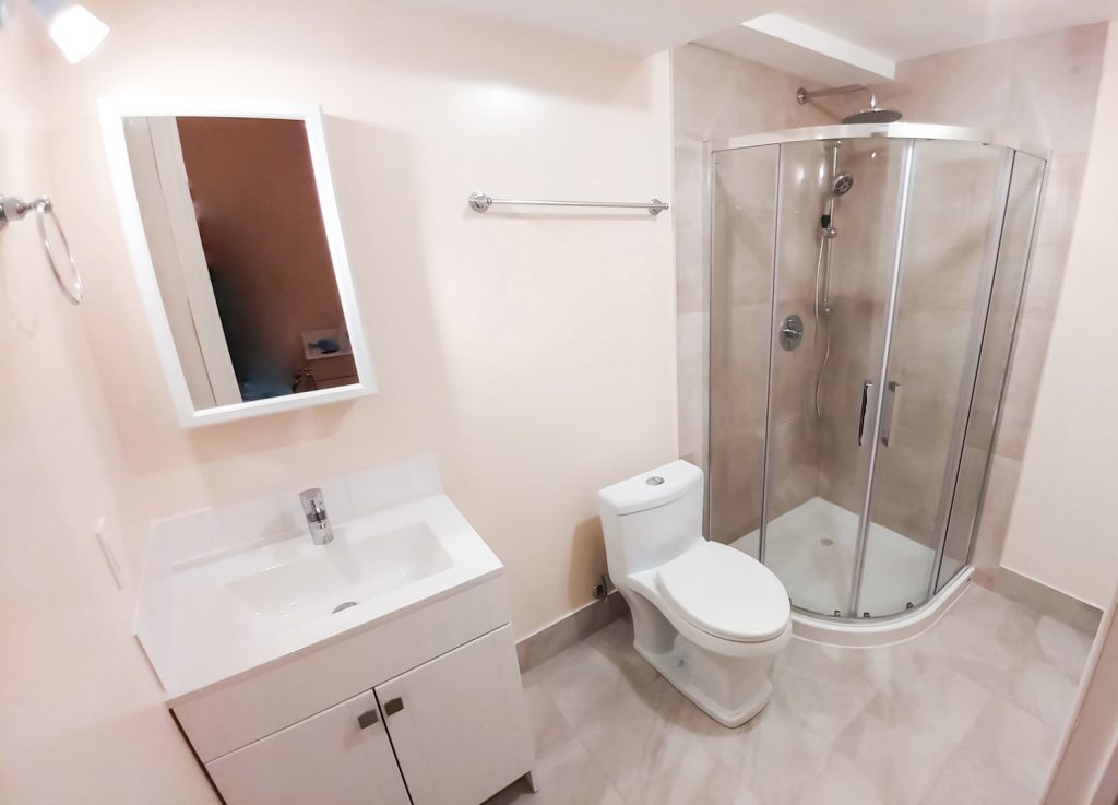 Compact bathroom with a white vanity, toilet and corner glass shower