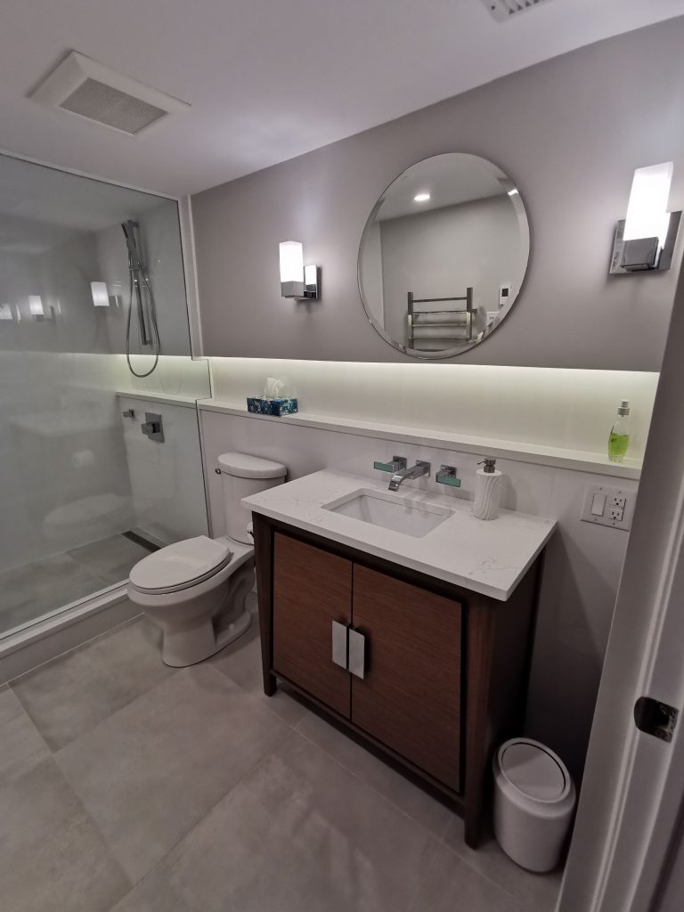 Custom bathroom renovation with brown vanity and backlit storage