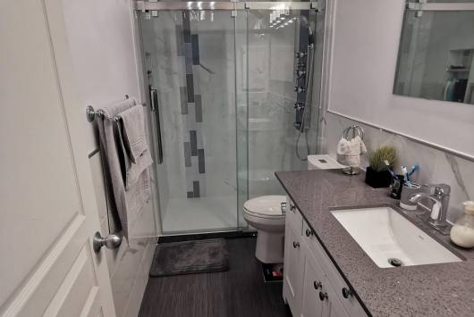 Renovated bathroom with a glass shower enclosure, white vanity and grey countertop