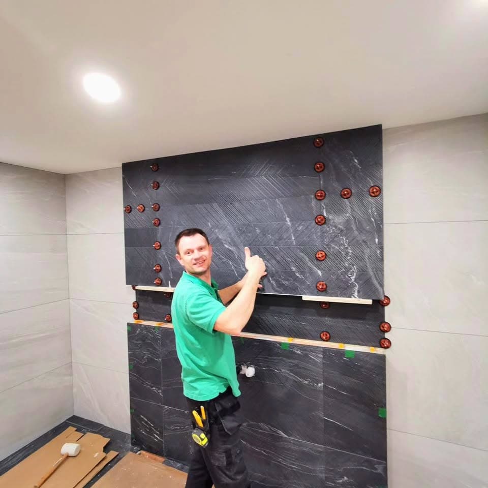 Bathroom renovator installing dark feature wall tiles with a tile levelling system
